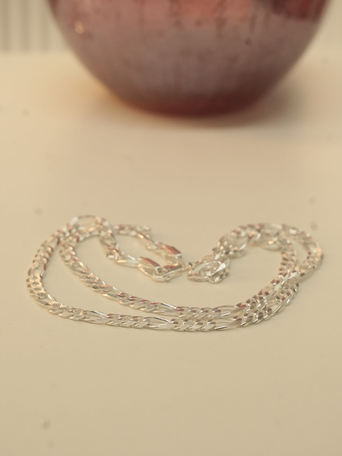 The silver figaro chain laid in loops beside a dark red glass vase.