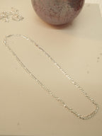 The silver figaro chain laid out in a long oval to show how it falls.