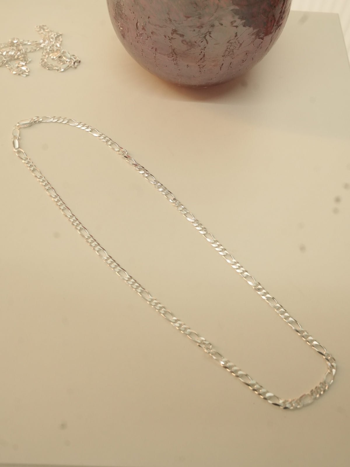 The silver figaro chain laid out in a long oval to show how it falls.