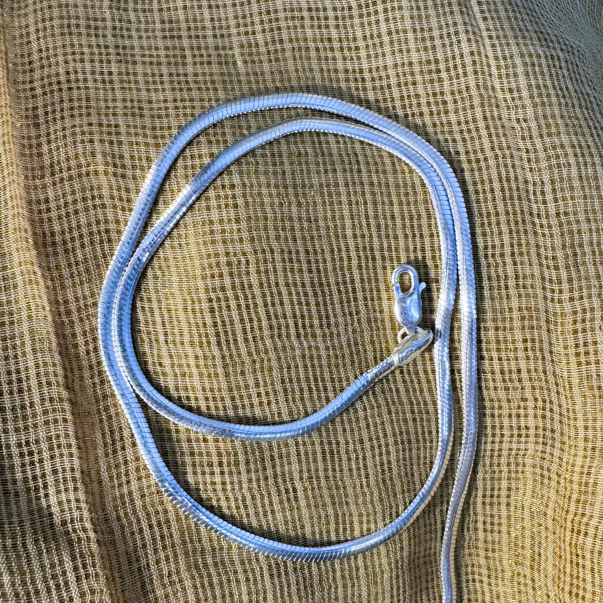 The silver herringbone chain coiled on pale fabric.