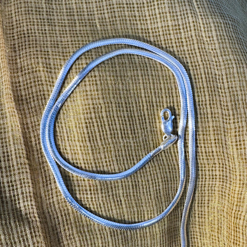 The silver herringbone chain coiled on pale fabric.