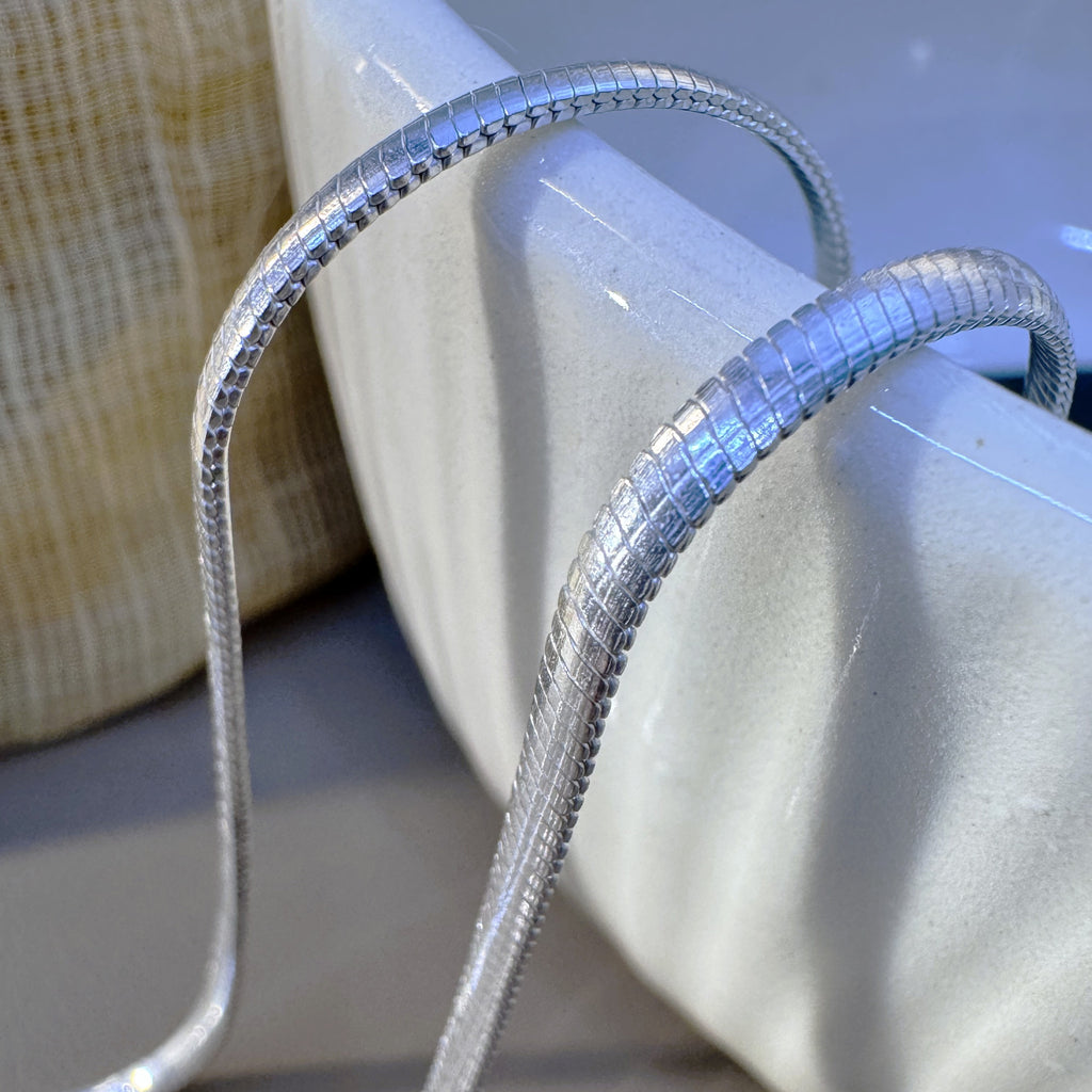 The silver herringbone chain draped over the rim of a white bowl.