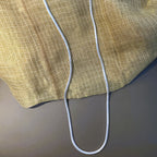 The silver herringbone chain hanging full length against cream fabric.