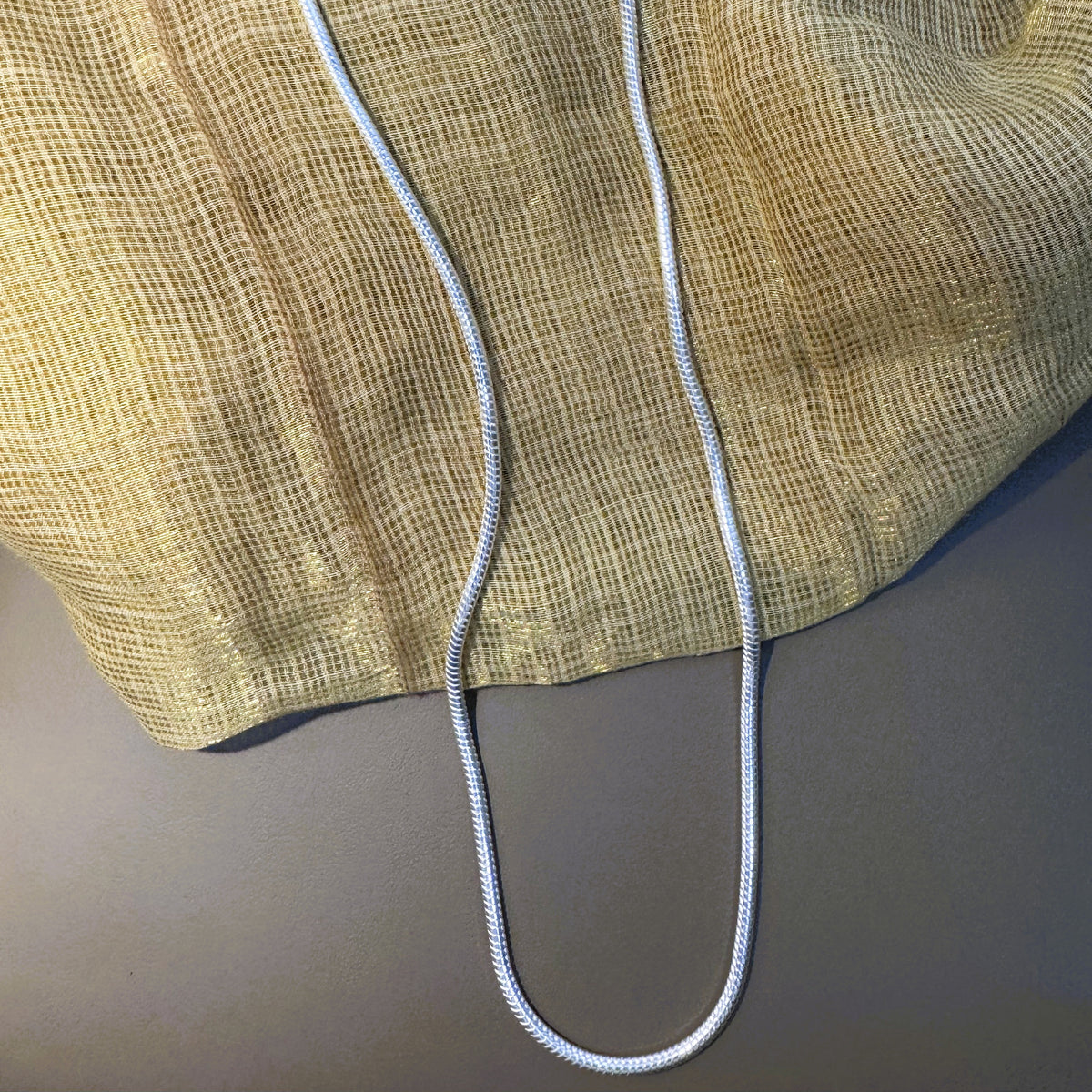 The silver herringbone chain hanging full length against cream fabric.