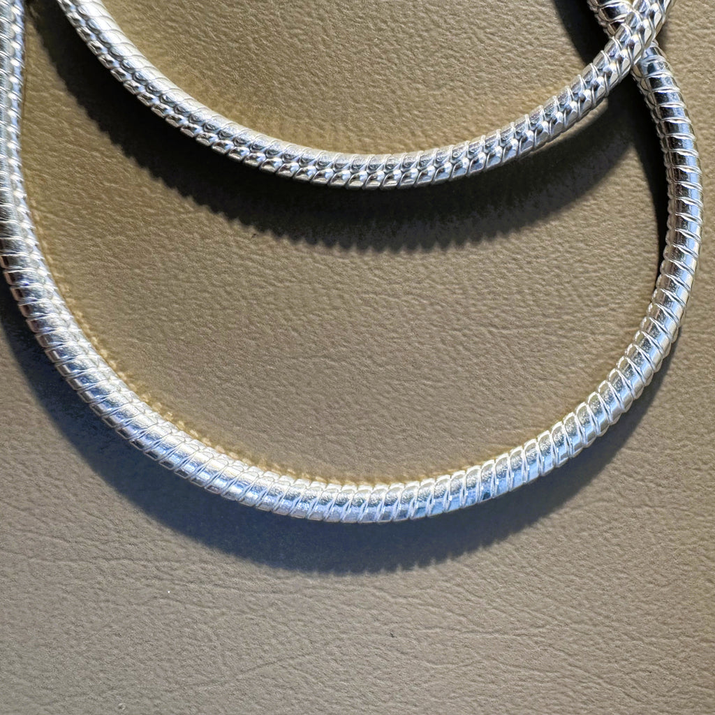 Sterling silver omega snake chain lying in two loops on a tan surface.