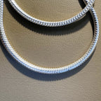 Sterling silver omega snake chain lying in two loops on a tan surface.