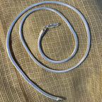 The omega snake chain coiled on cream fabric with the lobster clasp at the top.
