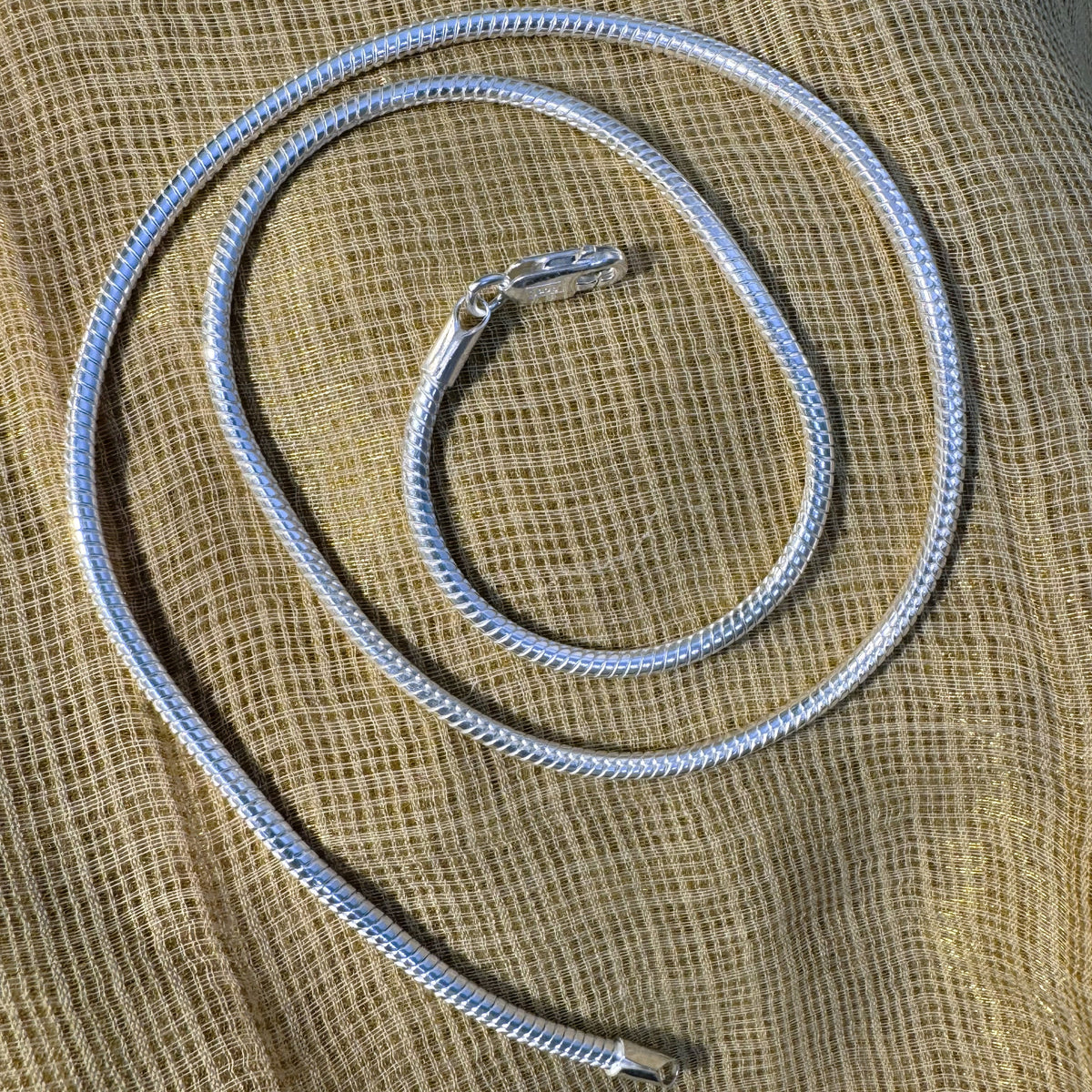 The omega snake chain coiled on cream fabric with the lobster clasp at the top.