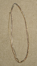 Triple-strand chain with silver, gold-tone and rose gold-tone faceted bar links, laid in an open oval on a beige textile backdrop.