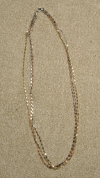 Triple-strand chain with silver, gold-tone and rose gold-tone faceted bar links, laid in an open oval on a beige textile backdrop.