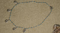 Sterling silver chain with turquoise-blue enamel beads and six cowrie shell drops set with cubic zirconia, laid flat on a beige woven backdrop.
