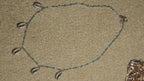 Sterling silver chain with turquoise-blue enamel beads and six cowrie shell drops set with cubic zirconia, laid flat on a beige woven backdrop.
