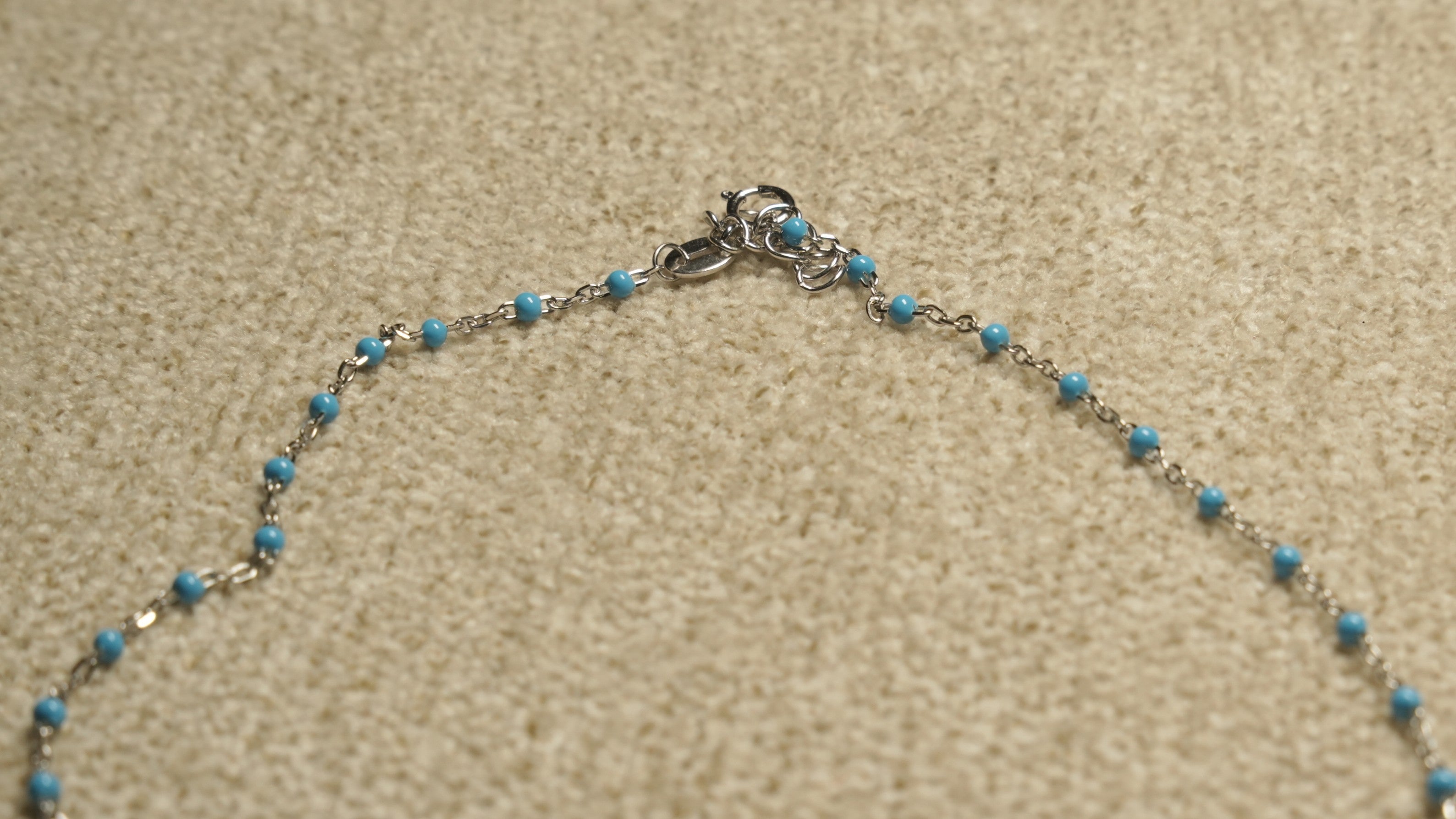 Close view of the spring-ring clasp and turquoise-blue beaded sections of the sterling silver shell chain.