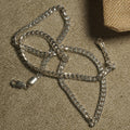 Bevelled sterling silver curb chain with flat interlocking links arranged on beige fabric beside a woven jute pouch, lobster clasp open.