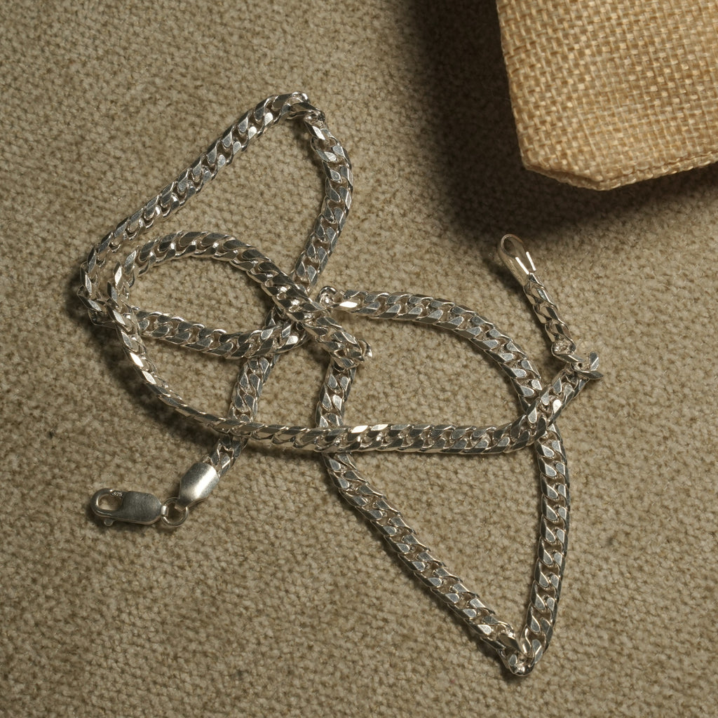 Polished curb chain in sterling silver laid in loose loops, showing its flat facet-cut links and lobster clasp stamped 925.