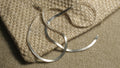 Flat sterling silver herringbone chain draped in soft curves across the corner of a woven jute pouch.