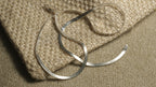 Flat sterling silver herringbone chain draped in soft curves across the corner of a woven jute pouch.