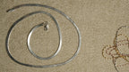 Sterling silver herringbone chain coiled on a beige textile, with fine tri-tone chains visible at the edge of the frame.