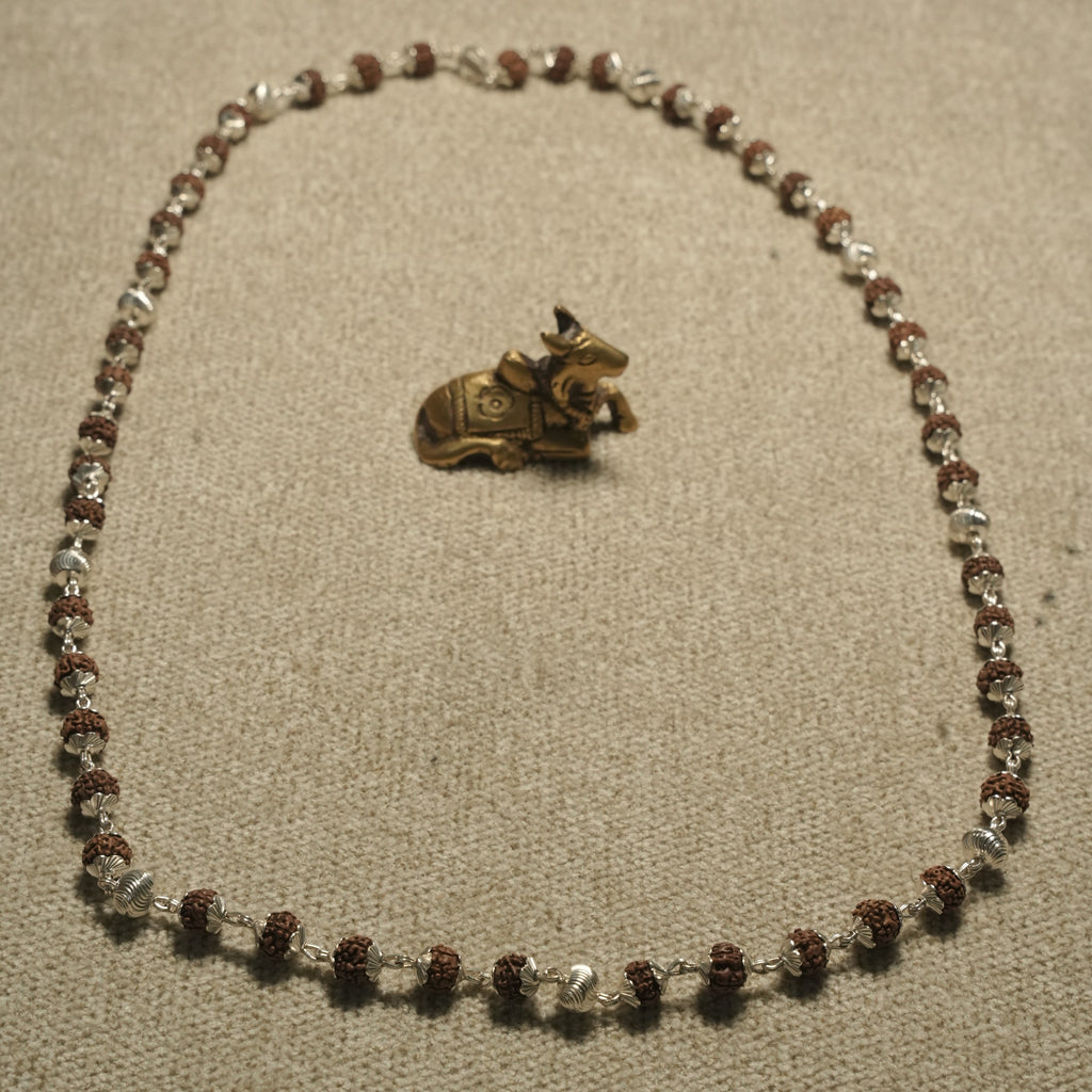 Full 65 cm Rudraksha chain laid open in an oval beside a small brass Nandi figurine.