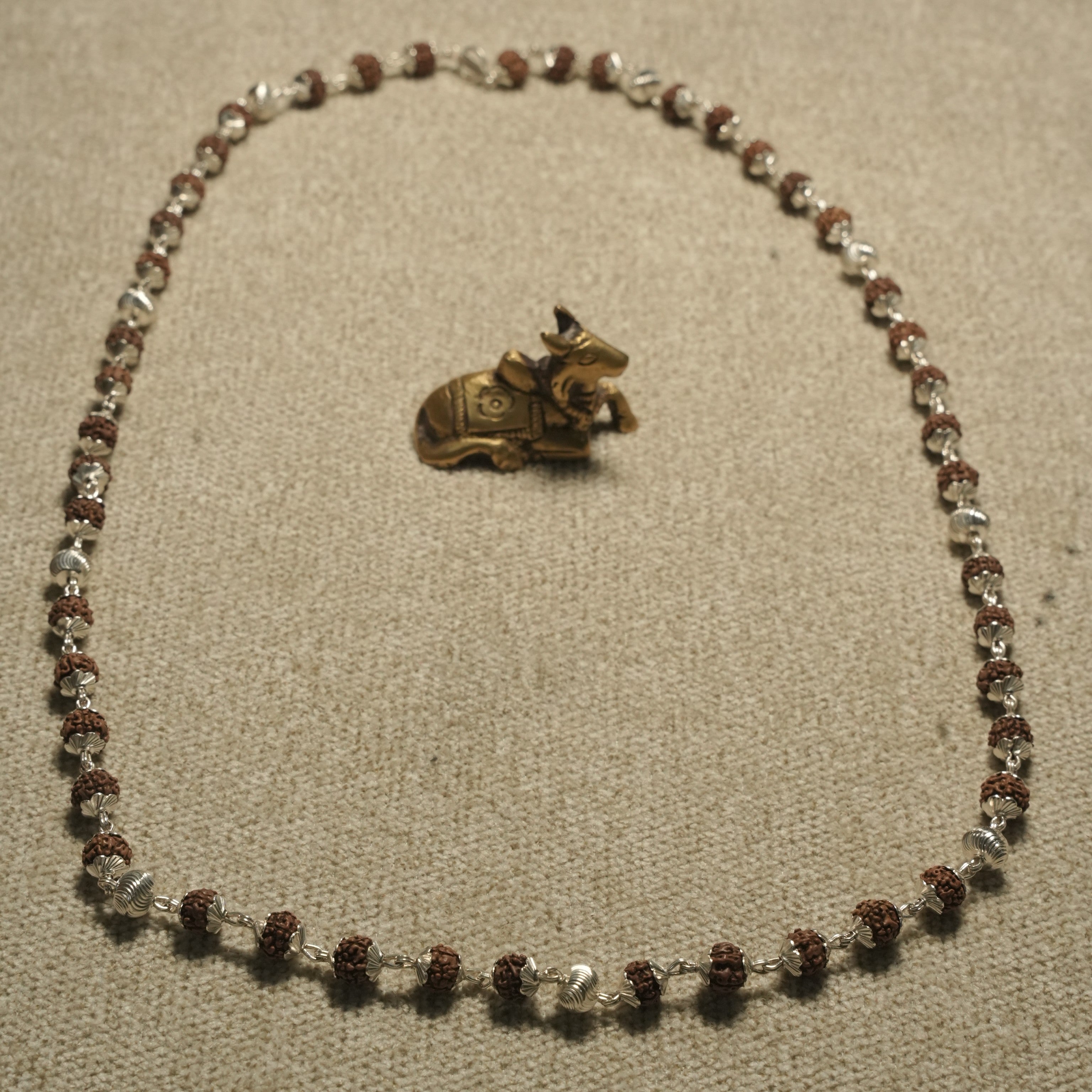 Full 65 cm Rudraksha chain laid open in an oval beside a small brass Nandi figurine.