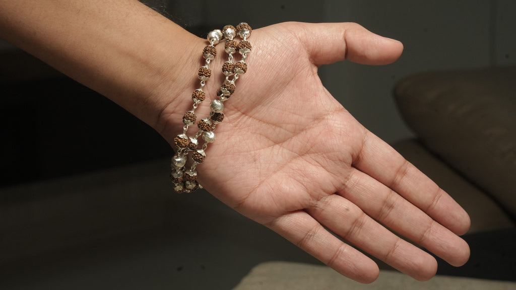Rudraksha and silver bead chain draped in two wraps across an open palm to show its length.
