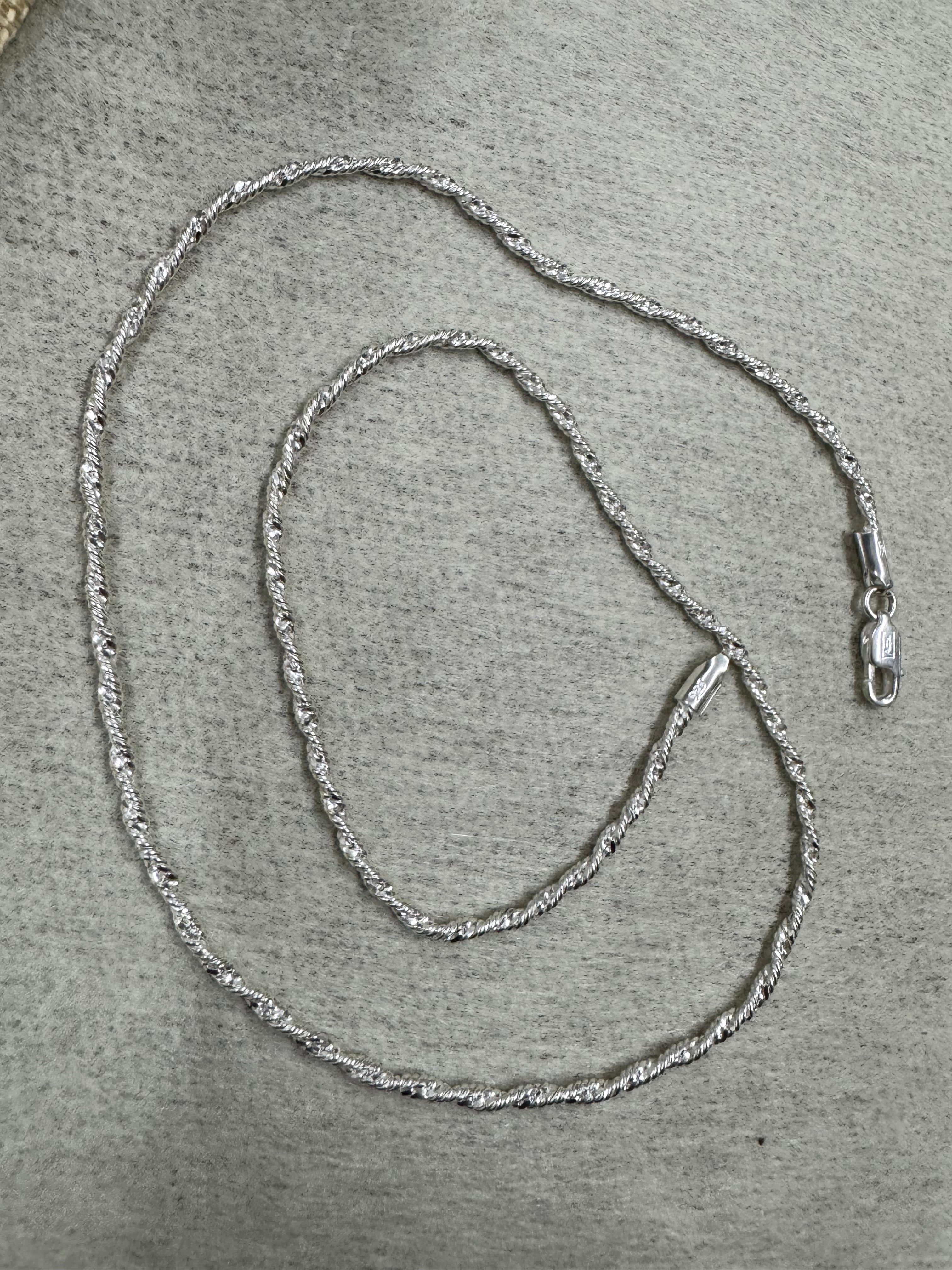 Full 50 cm length of the sterling silver Singapore chain necklace laid in loops on grey felt, with the lobster clasp at the right.