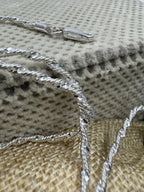 Sterling silver Singapore chain necklace draped over a dotted cream cushion, with the open lobster clasp resting above it.