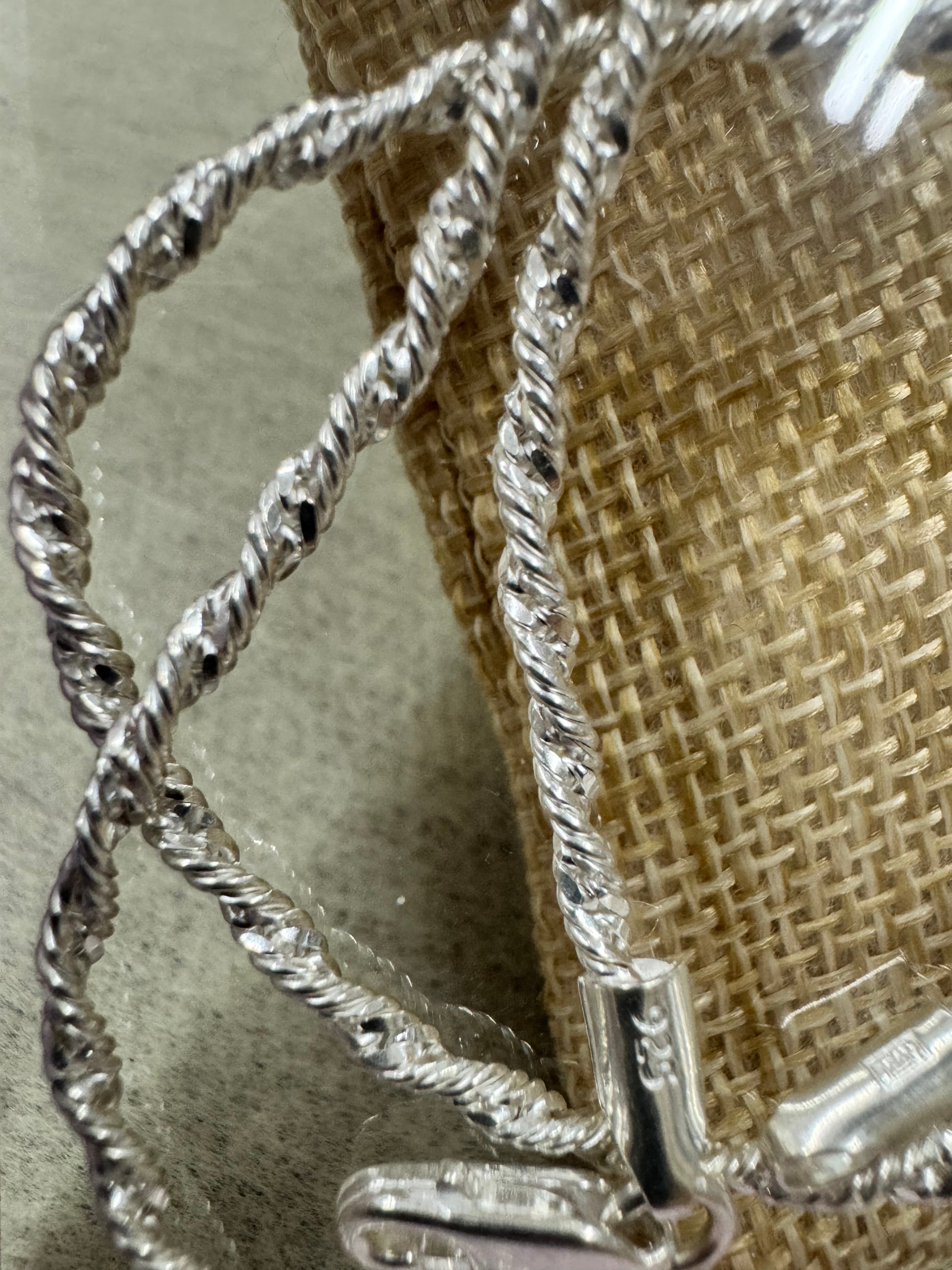 Close view of the sterling silver chain crossing over itself on jute, showing the spiral of the twist and the end tag below.