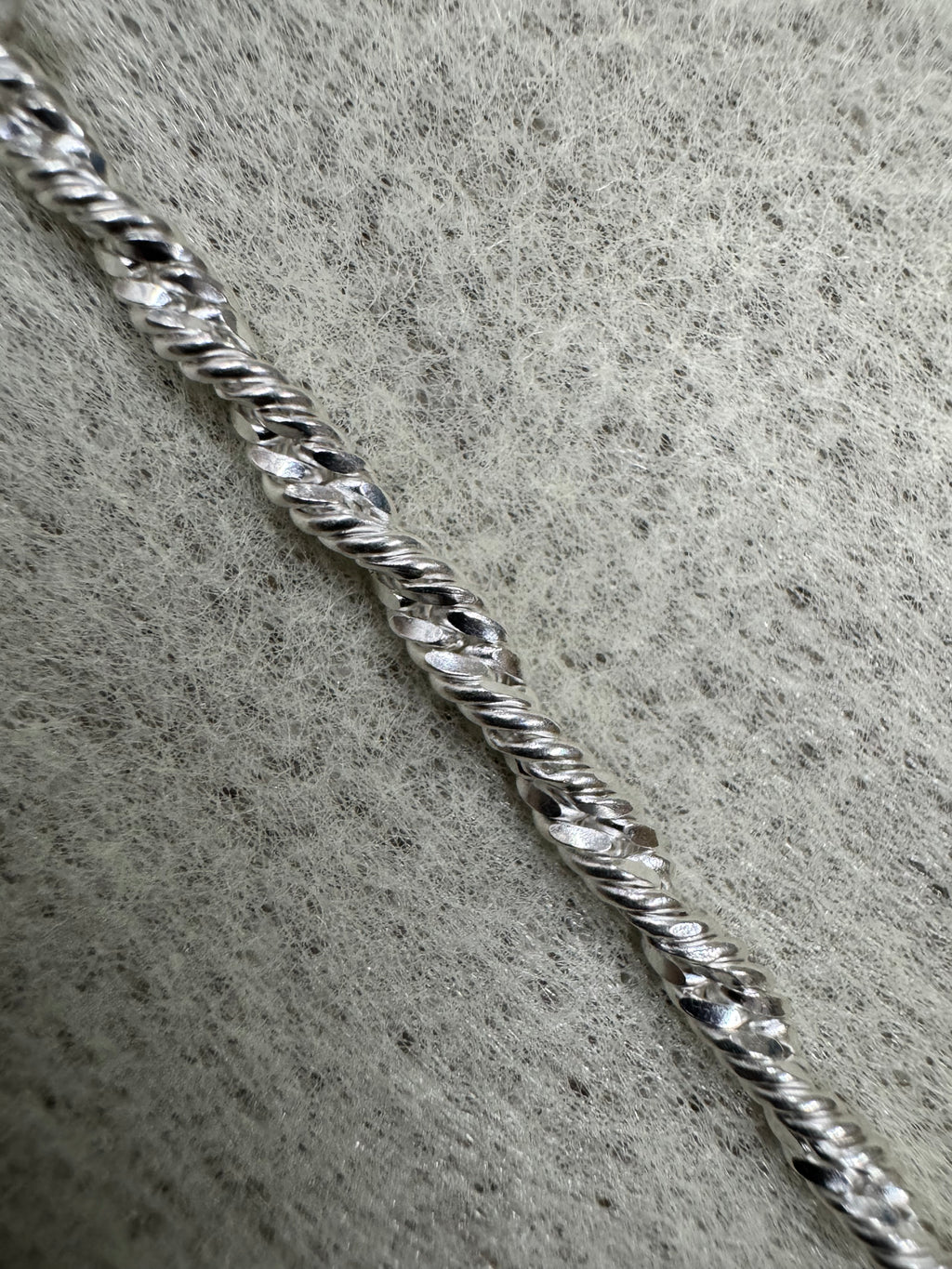 Single strand of the sterling silver Singapore chain photographed close on grey felt, showing the diamond-cut facets along the twist.