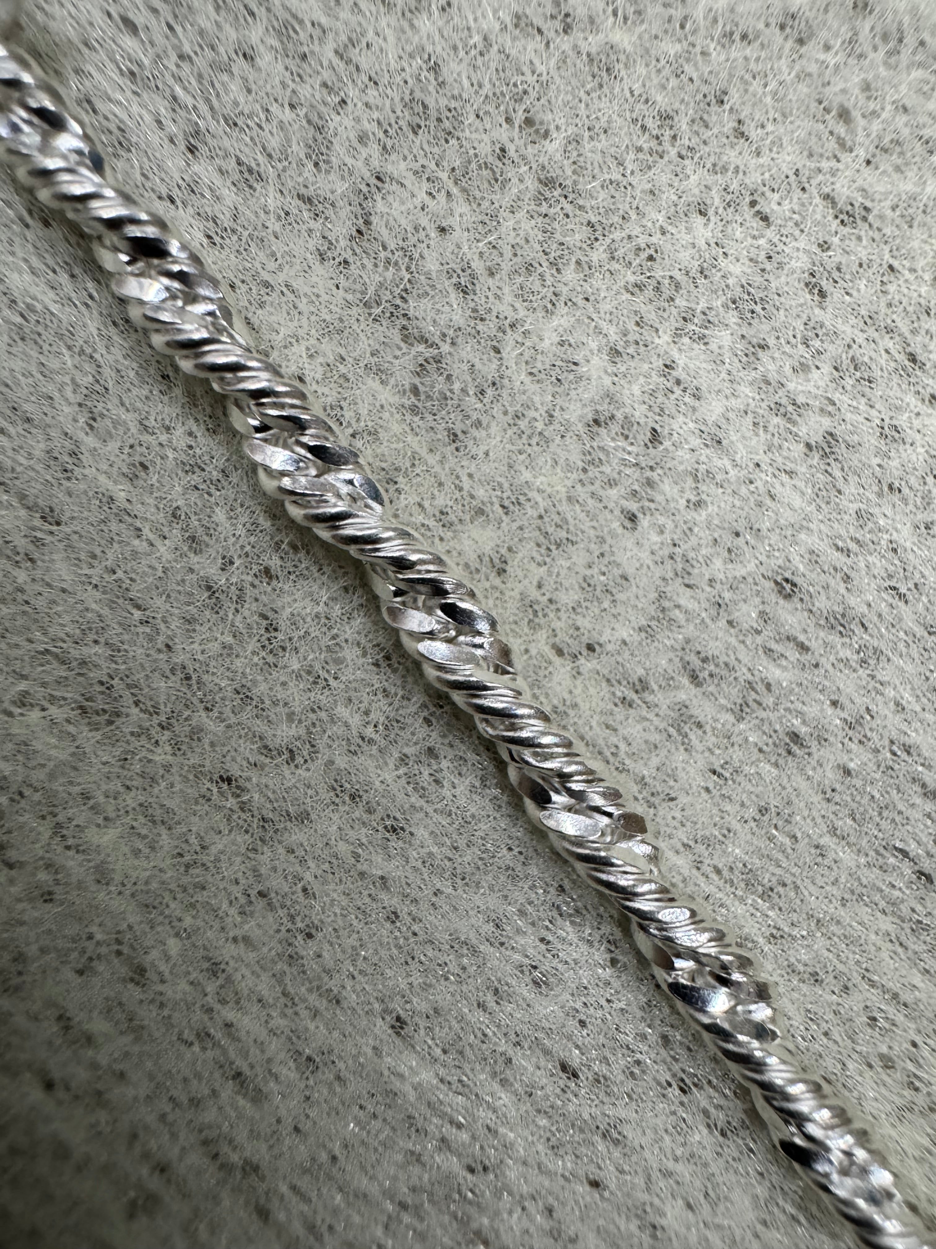 Single strand of the sterling silver Singapore chain photographed close on grey felt, showing the diamond-cut facets along the twist.