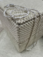 Sterling silver Singapore chain necklace coiled on a cream textured cushion, the clasp at the top and the chain falling over the edge.