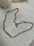 Multi-strand sterling silver box chain necklace in silver, gold-tone and rose-tone finishes, laid in a loop on grey felt.
