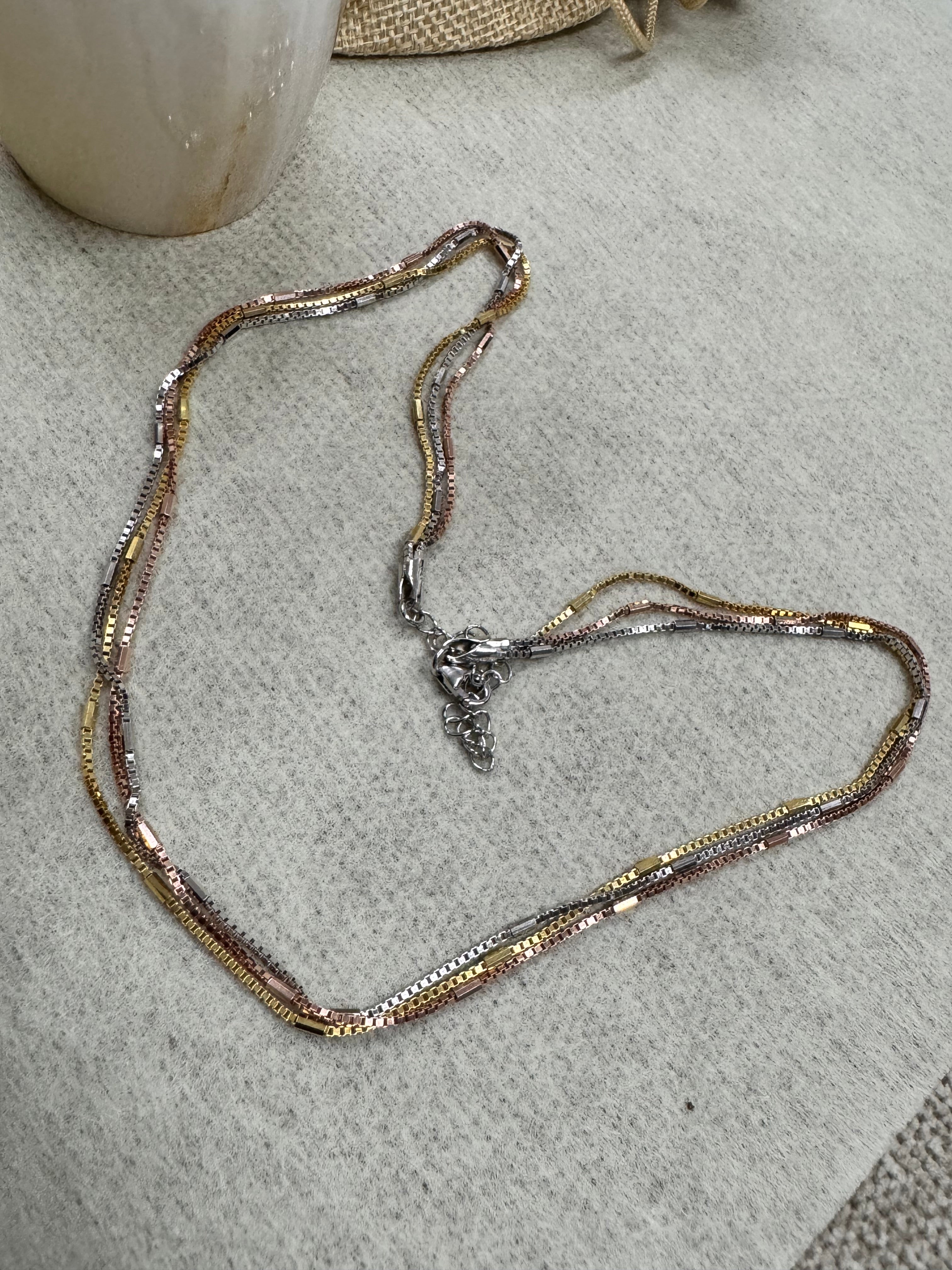 Multi-strand sterling silver box chain necklace in silver, gold-tone and rose-tone finishes, laid in a loop on grey felt.