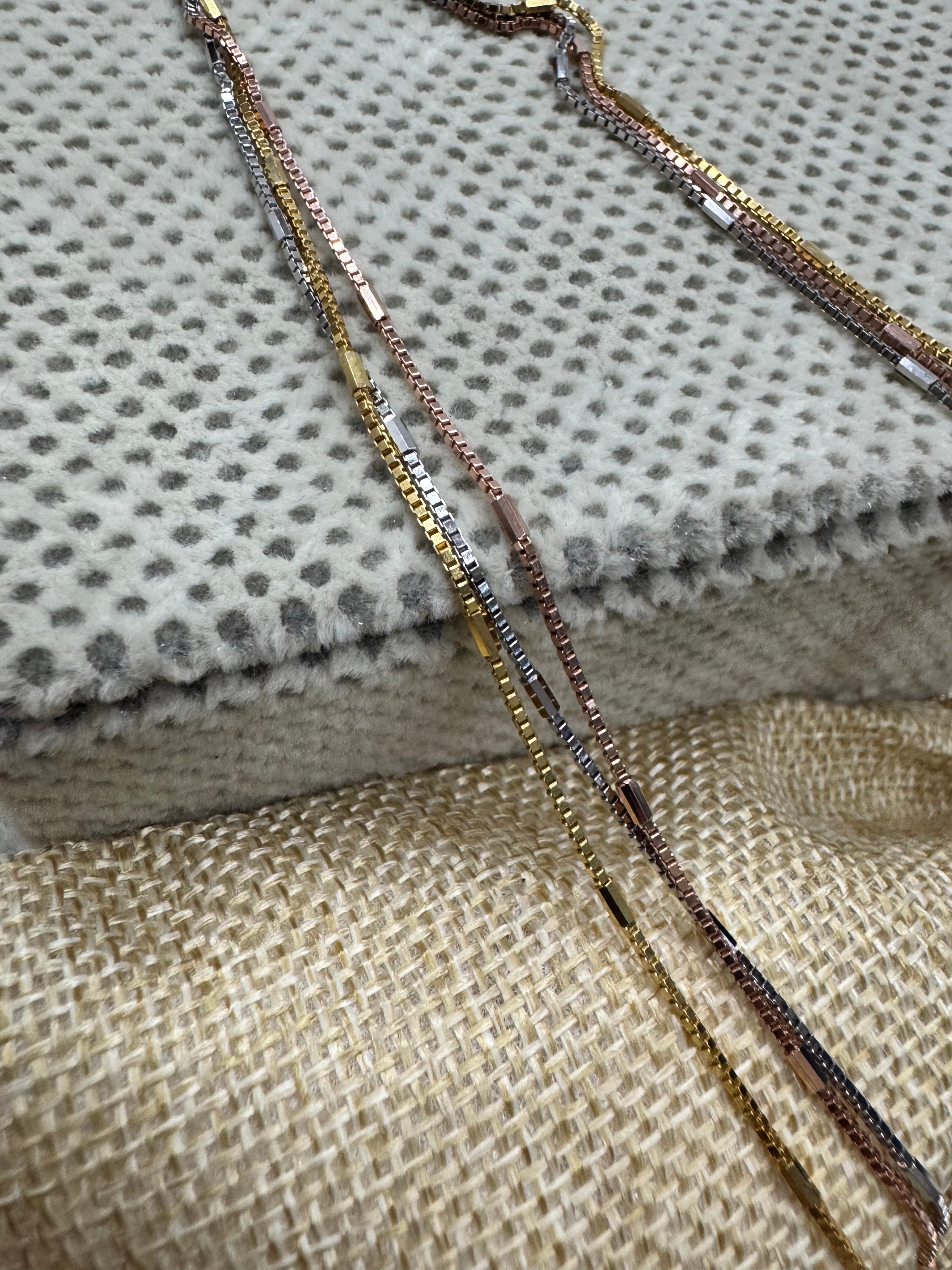 Strands of the sterling silver box chain necklace crossing a cream blanket and a jute pouch.