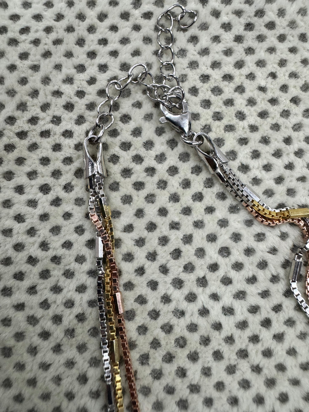 Lobster clasp and extender chain of the multi-strand sterling silver box chain necklace on spotted cream fabric.