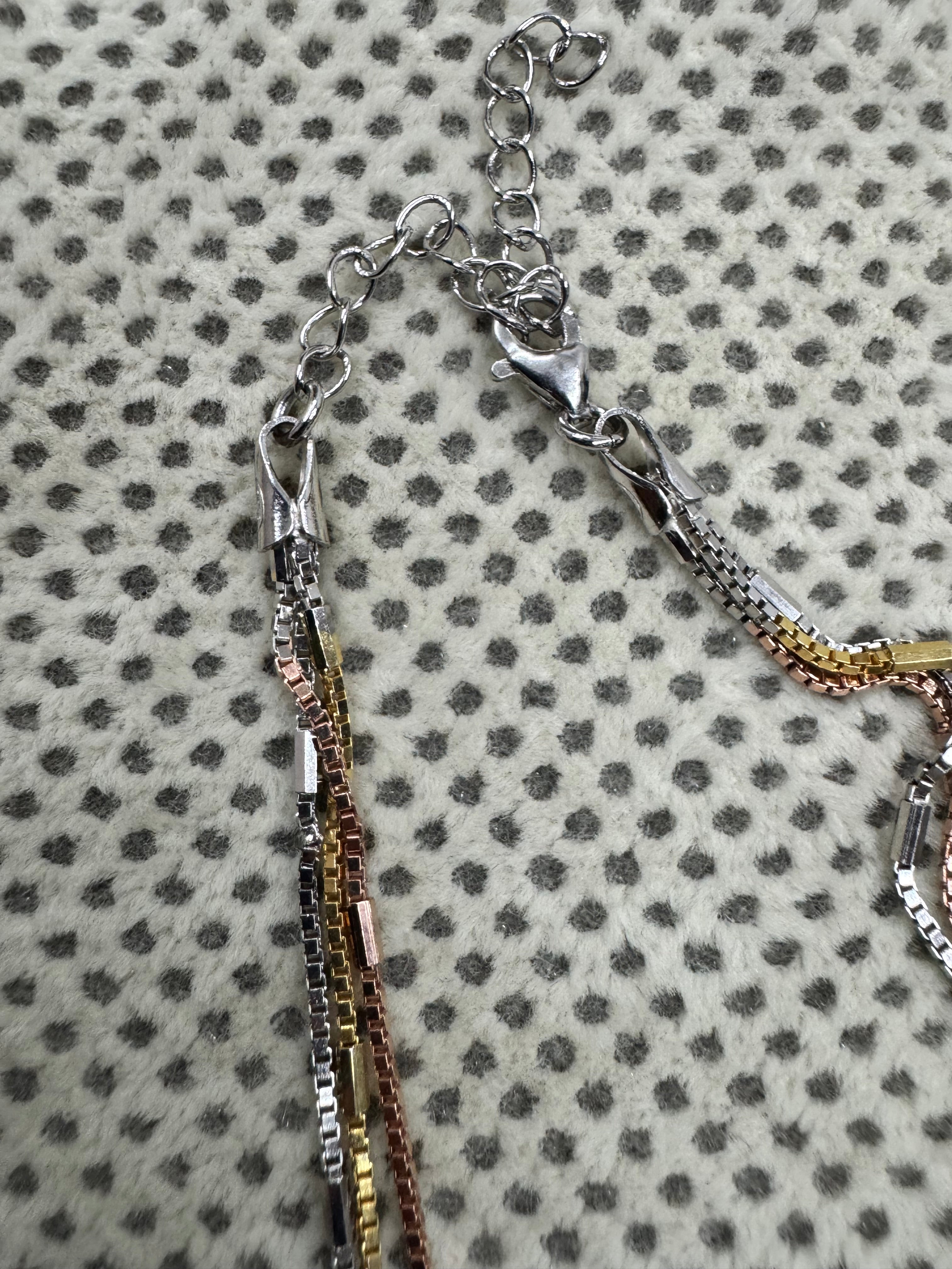 Lobster clasp and extender chain of the multi-strand sterling silver box chain necklace on spotted cream fabric.
