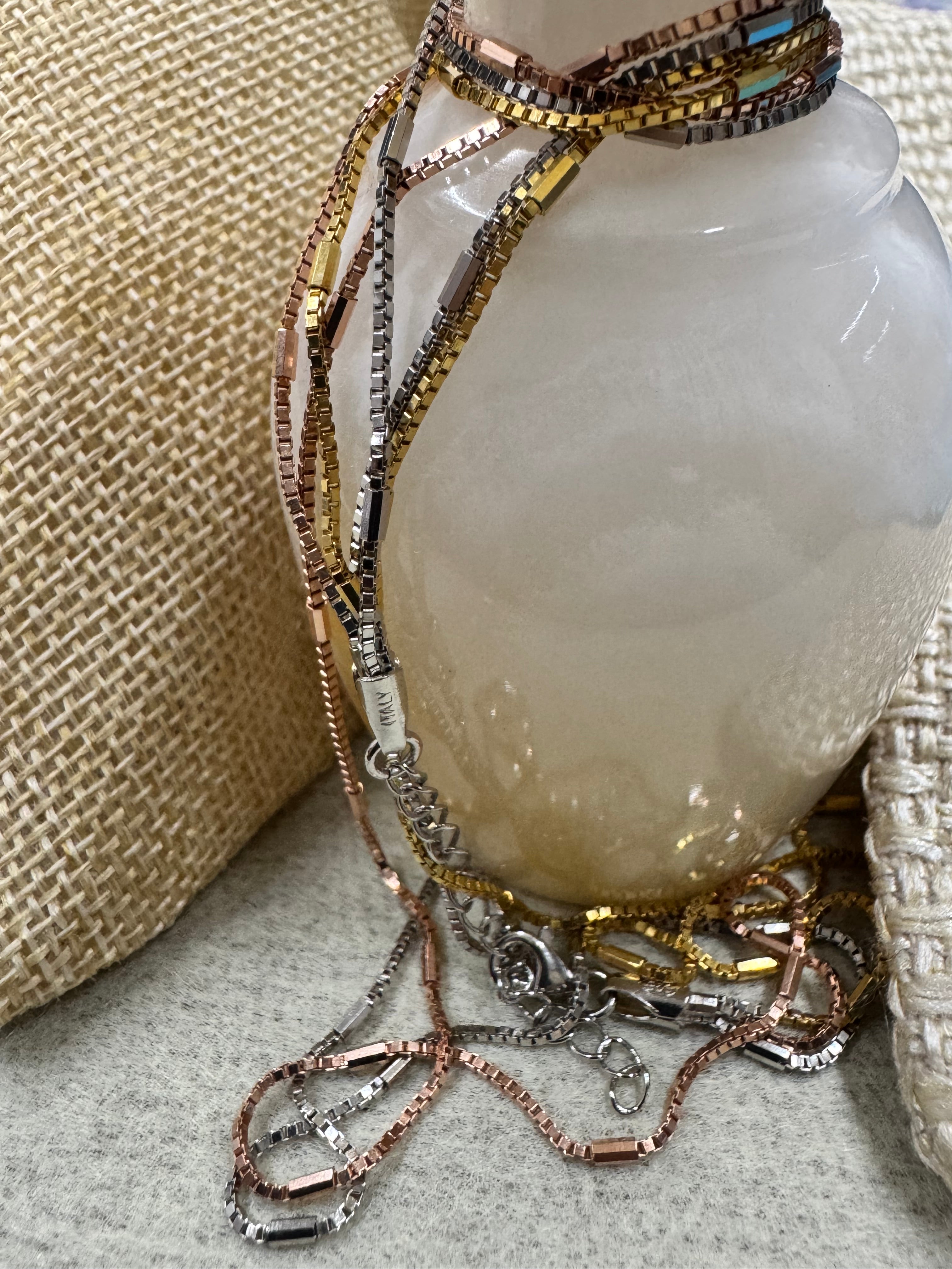 Sterling silver multi-strand box chain necklace resting against a pale polished vase, clasp and extender visible.