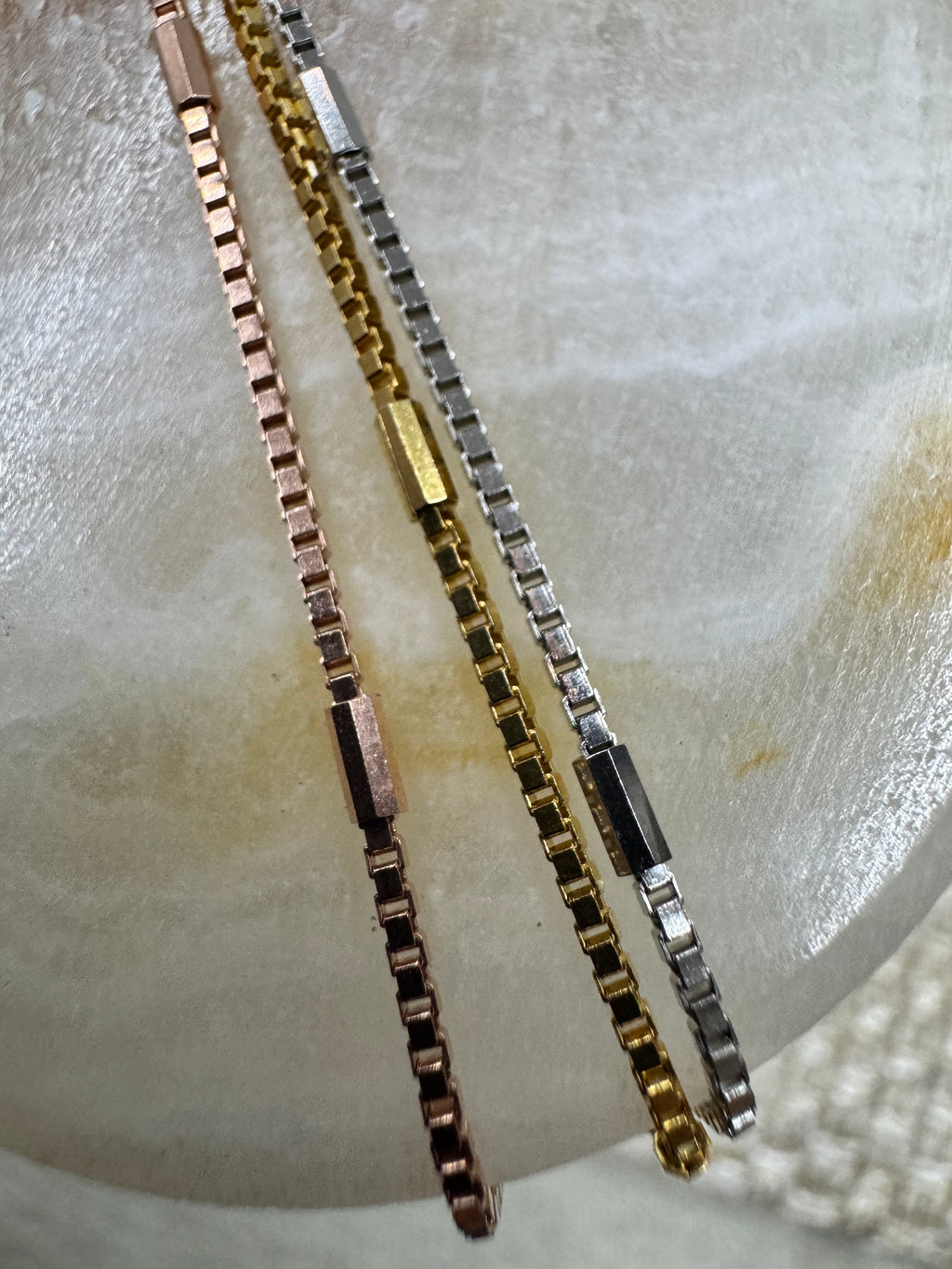 Three strands of the sterling silver box chain necklace in silver, gold-tone and rose-tone, each broken by a longer flat bar link.