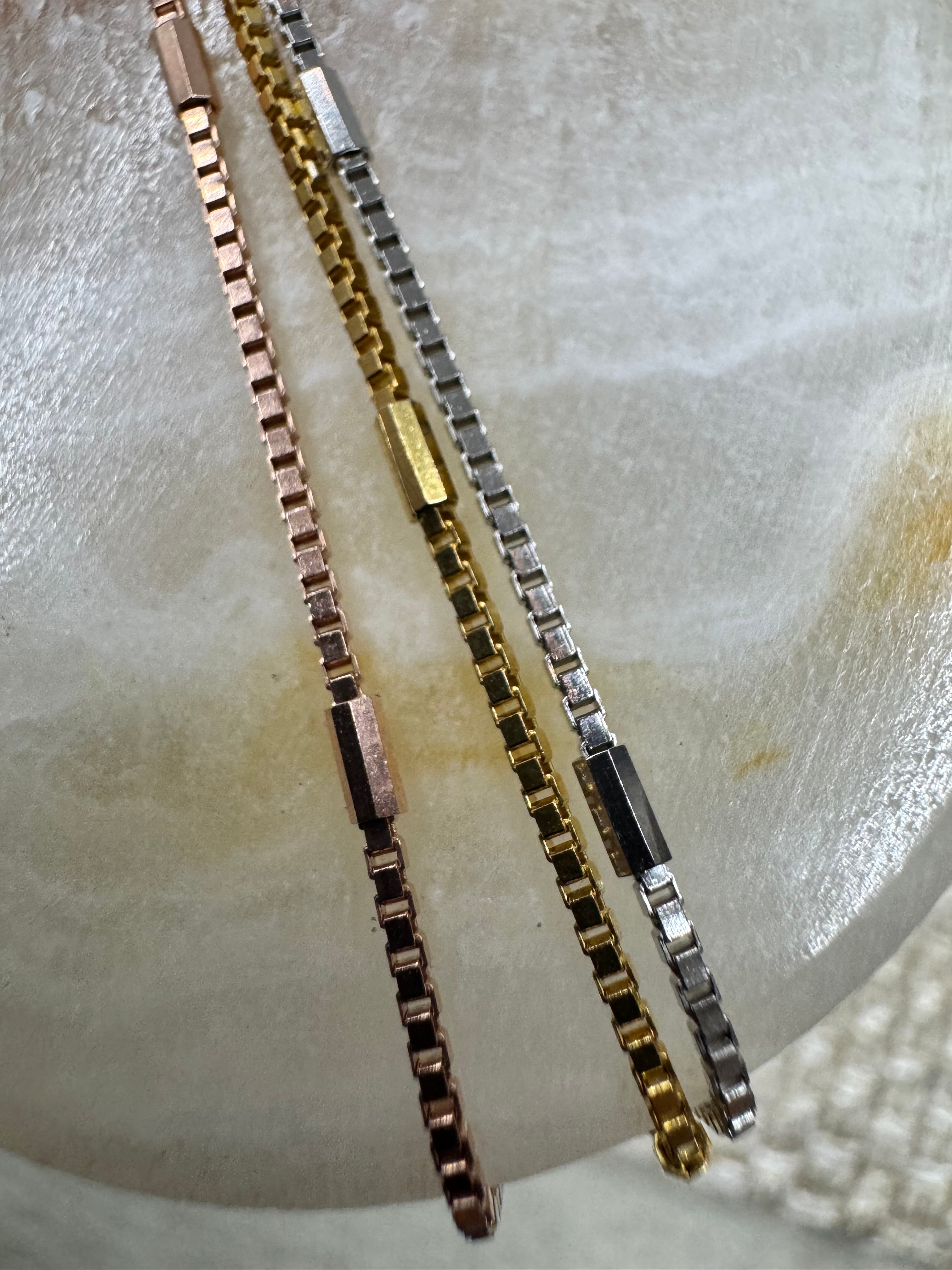 Three strands of the sterling silver box chain necklace in silver, gold-tone and rose-tone, each broken by a longer flat bar link.