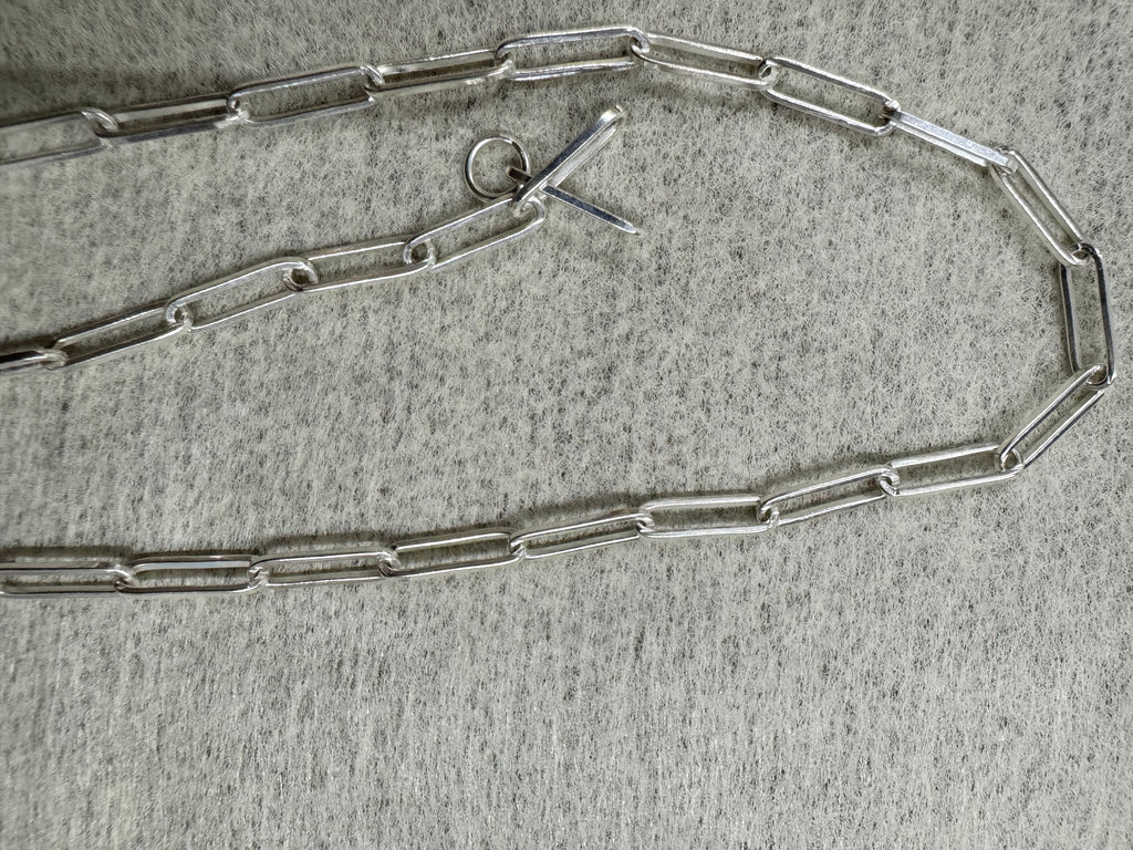 Sterling silver paperclip chain necklace laid open on grey felt with its T-bar and ring clasp at the centre.