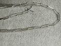 Sterling silver paperclip chain necklace laid open on grey felt with its T-bar and ring clasp at the centre.