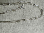 Sterling silver paperclip chain necklace laid open on grey felt with its T-bar and ring clasp at the centre.