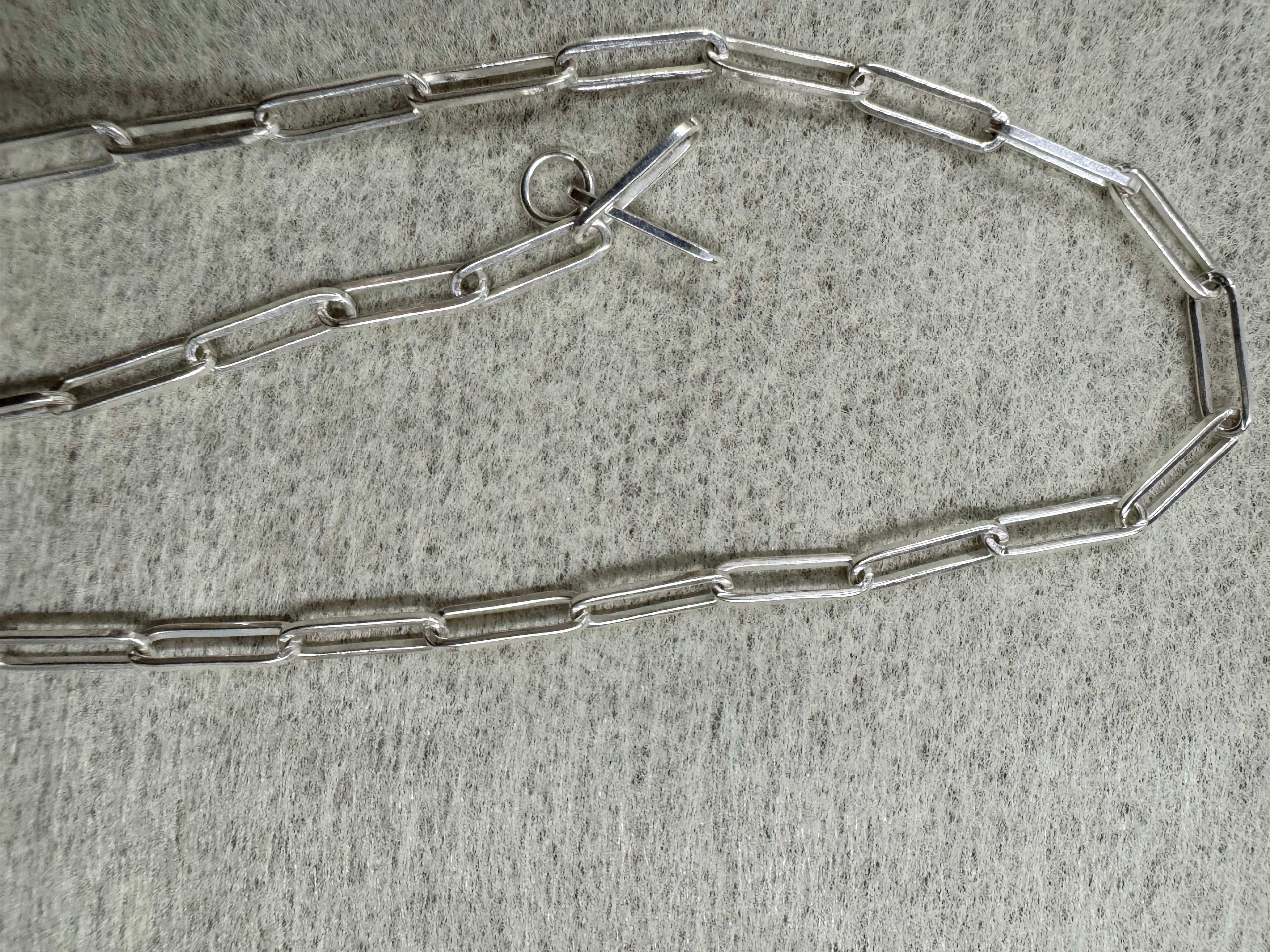 Sterling silver paperclip chain necklace laid open on grey felt with its T-bar and ring clasp at the centre.