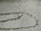 Full length of the sterling silver paperclip chain necklace curved on grey felt, T-bar and ring at the centre.