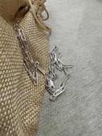Sterling silver paperclip chain necklace gathered loosely on a jute pouch and grey felt.