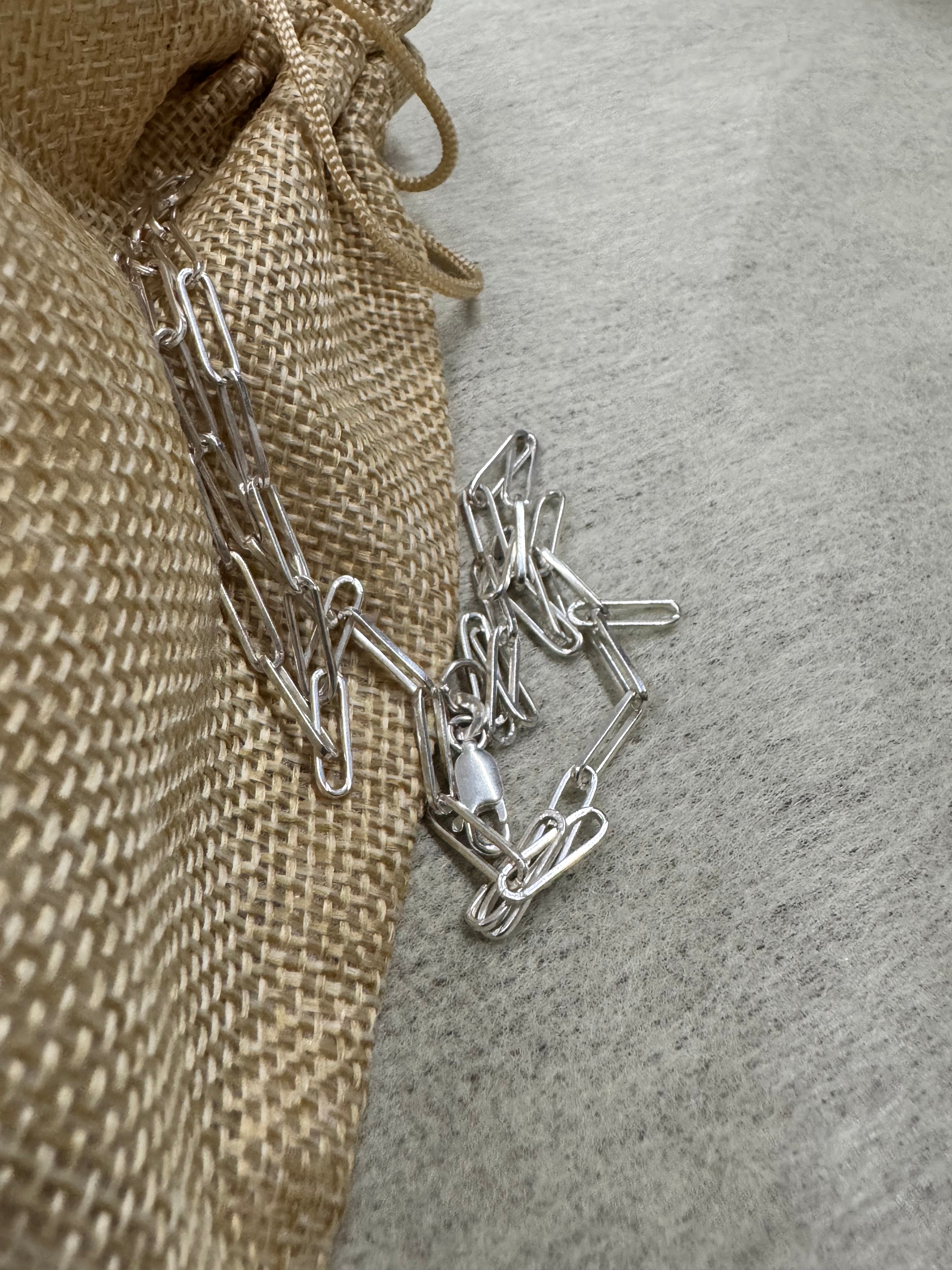 Sterling silver paperclip chain necklace gathered loosely on a jute pouch and grey felt.