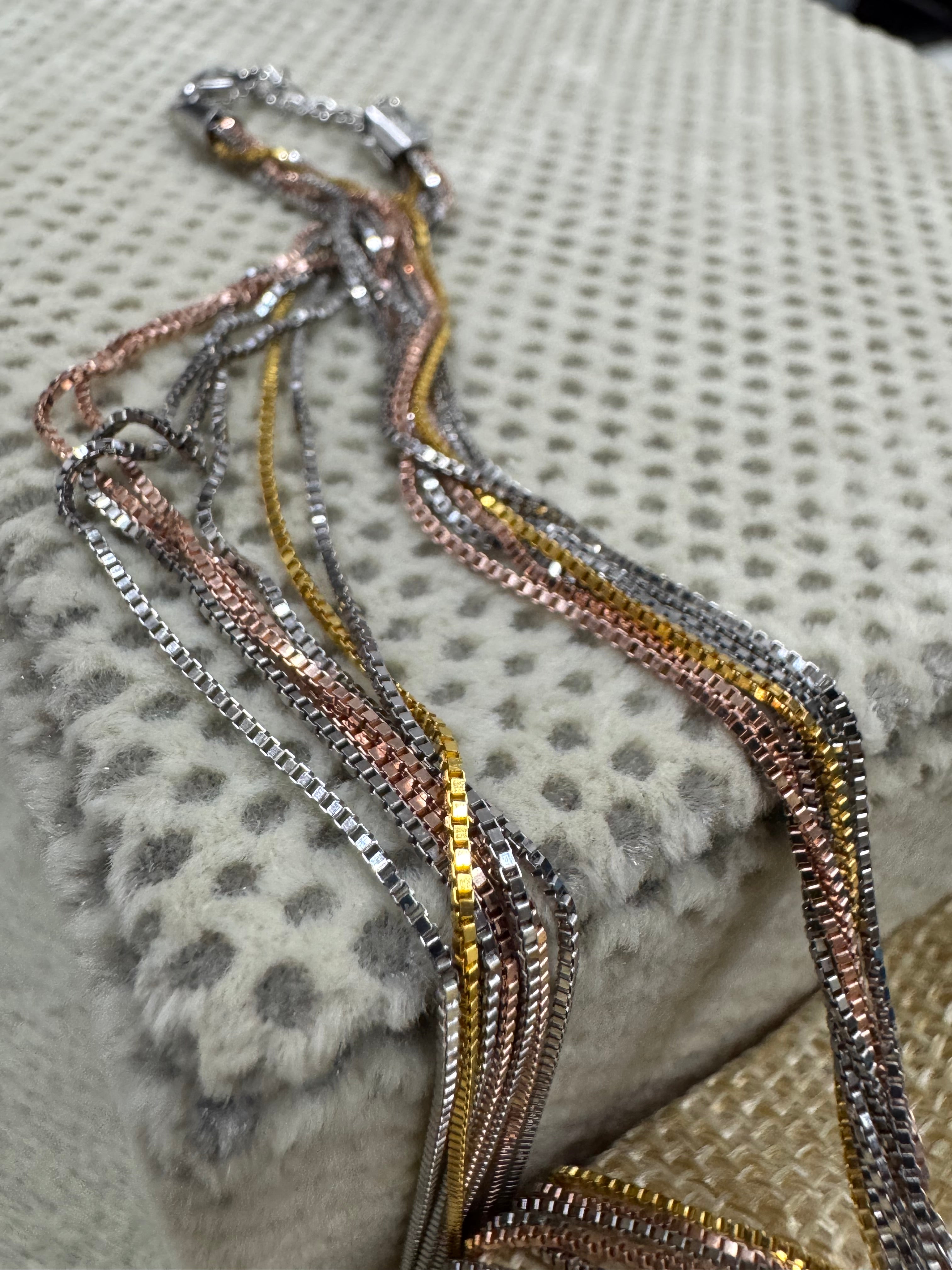 Strands of the sterling silver box chain necklace hanging from the end cap beside a jute pouch.