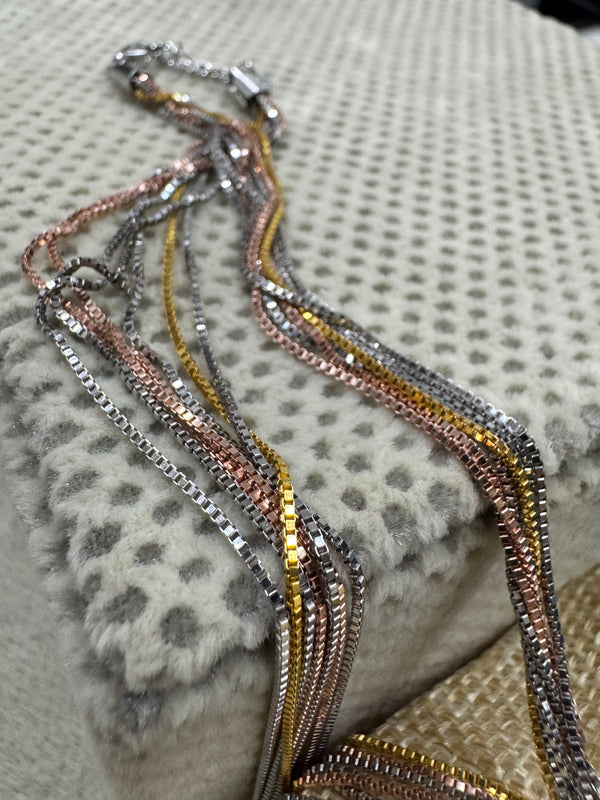 Strands of the sterling silver box chain necklace hanging from the end cap beside a jute pouch.