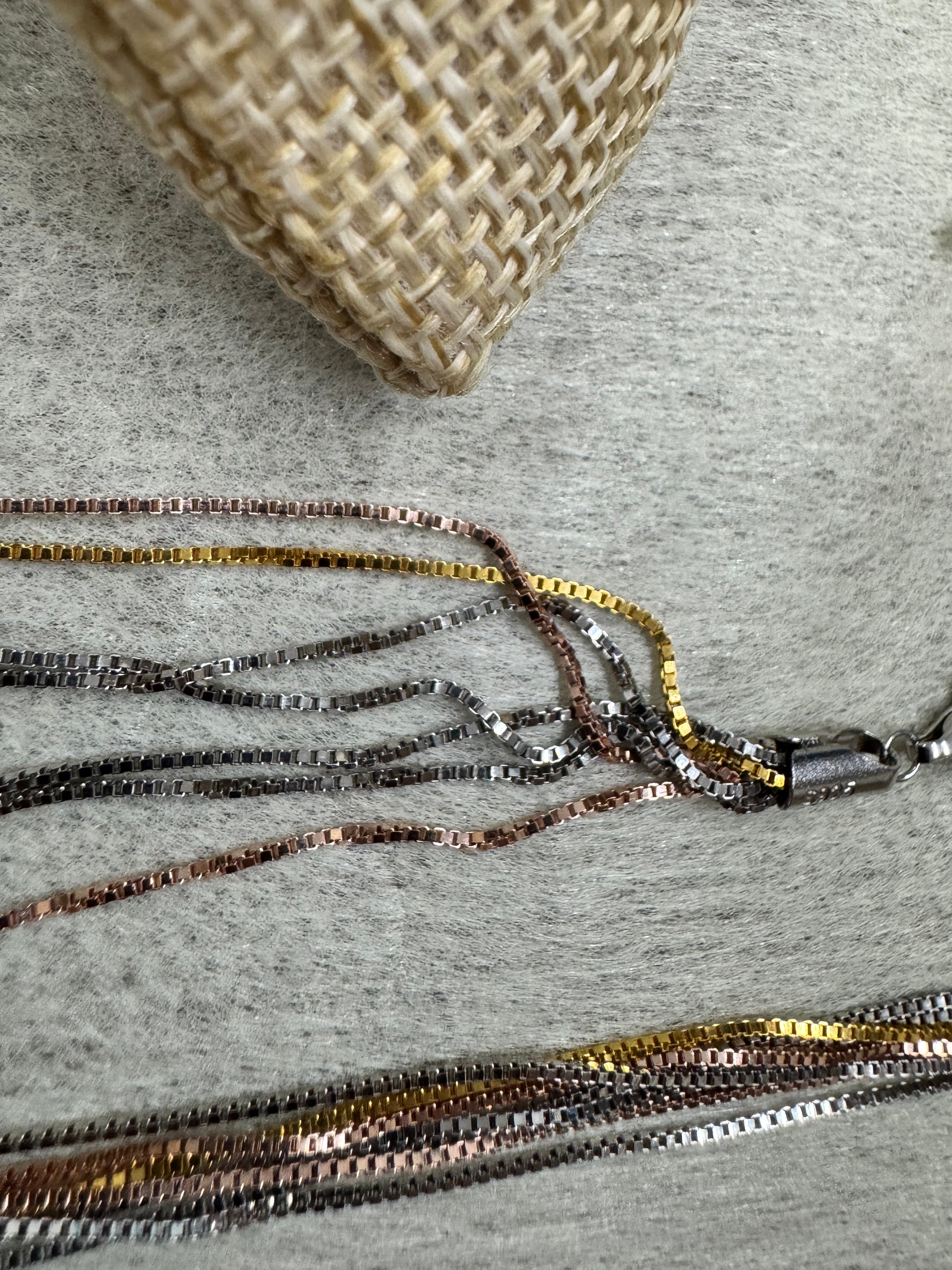 Sterling silver multi-strand box chain necklace draped over a cream blanket, clasp at the left.