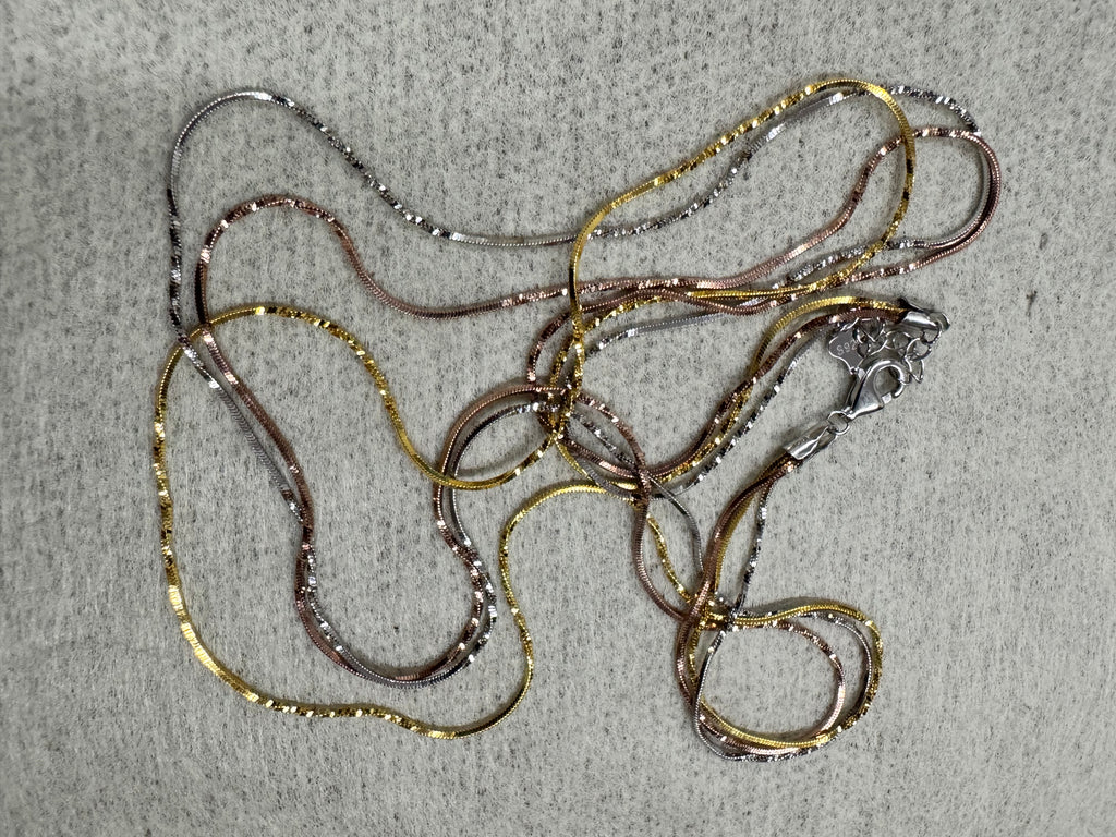 Tri-tone sterling silver three-strand snake chain necklace laid out full length on grey felt, 50 cm, with its lobster clasp.